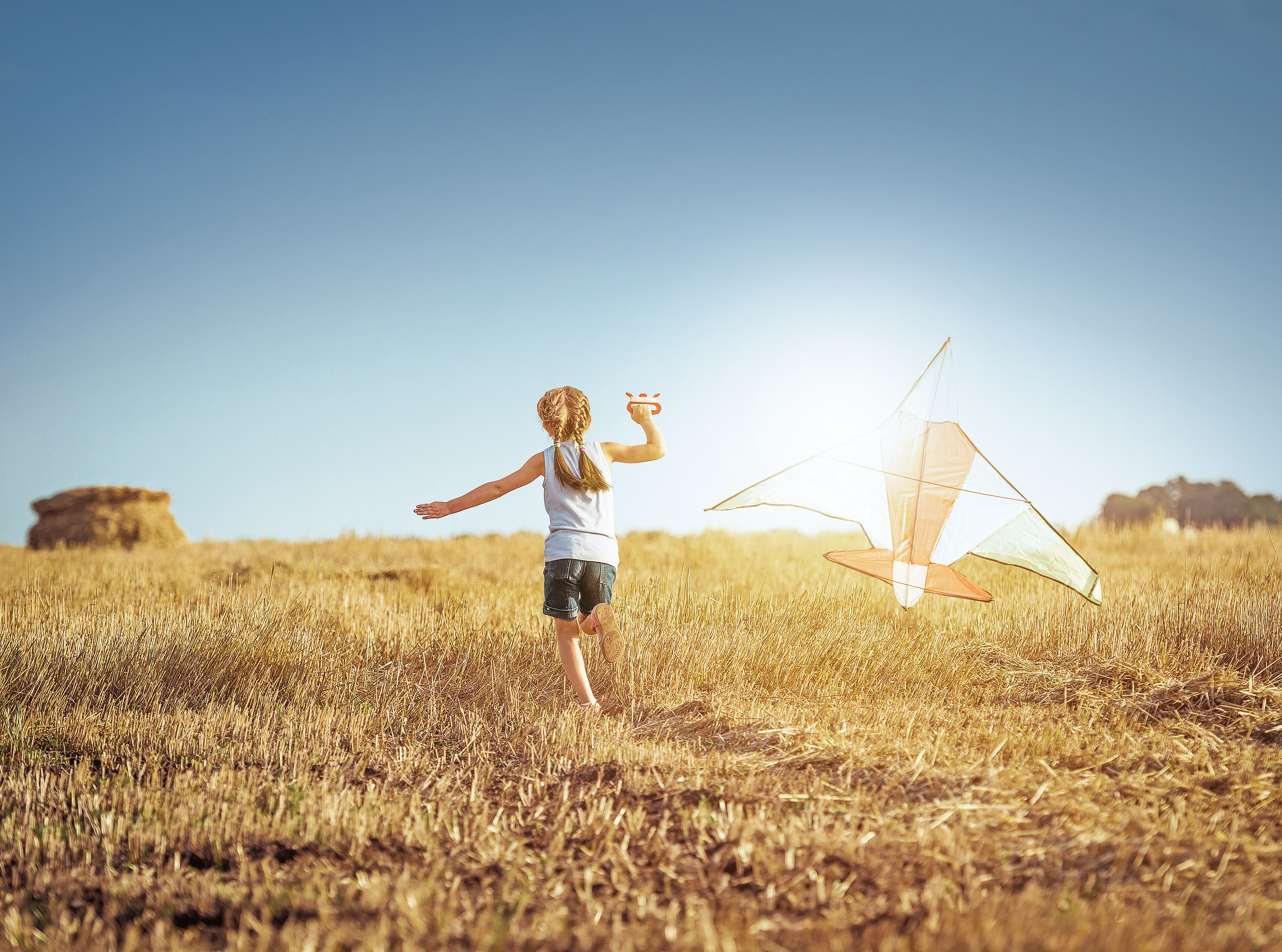 Kind läuft mit einem Drachen über ein Kornfeld